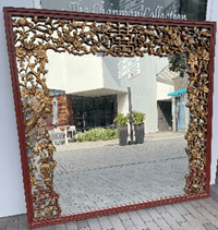 A mirror with a red frame and brown leaves.