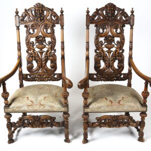 A pair of carved wood chairs with arms and backs.