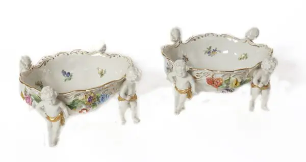 Two porcelain bowls with cherub legs and floral decor.