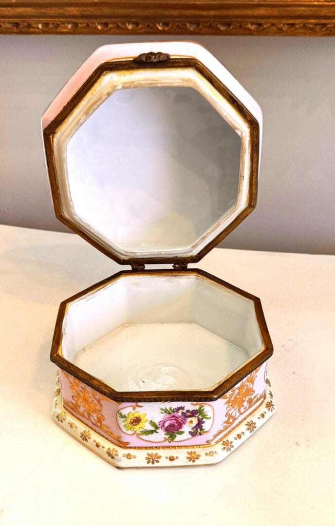 Open hinged lid of antique Sèvres style porcelain box showing white glazed porcelain interior and floral side panels