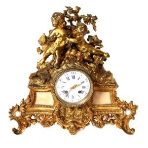 French Rococo-style mantel clock with sculpted putti beneath a grapevine canopy and blue Roman numerals at The Chapman Collection