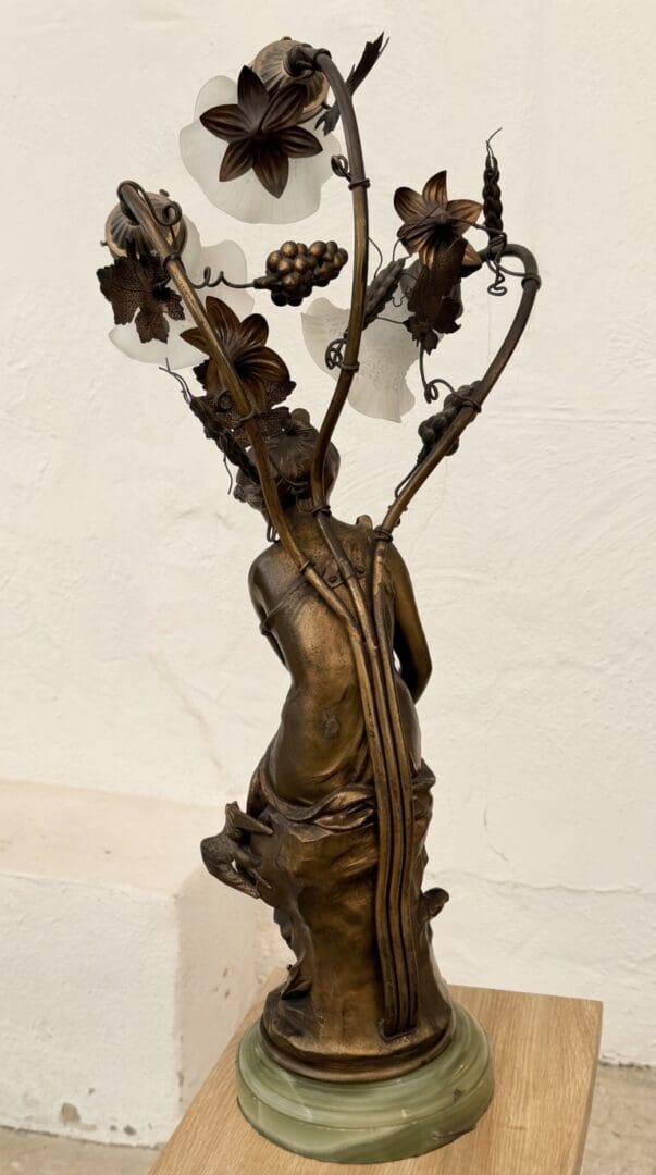 Back and side sculptural detail of French Art Nouveau figural lamp Hirondelle Blessee signed Moretay showing bronze grape clusters, wheat, leaves and frosted glass shades