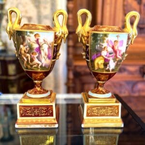 Elegant Pair of Royal Vienna Style Hand-Painted Porcelain Urns showing classical mythological scenes on a burgundy ground with 24-karat-style gilding, 11.75 inches high by 6.5 inches wide